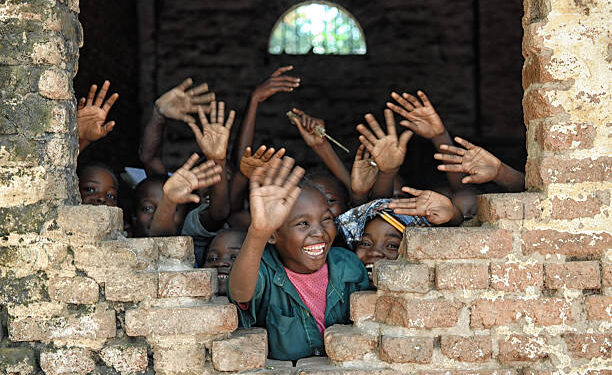 A group of african children inside of a destroyed school, wave hands and say hello.